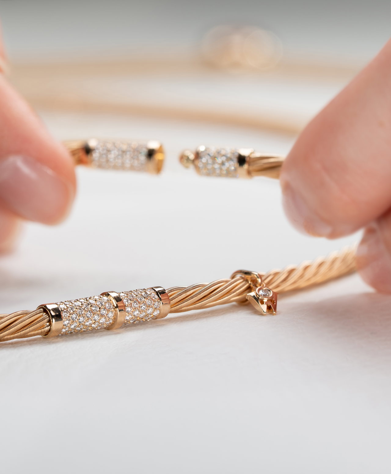 Zwei Händen halten ein goldenes Wellendorff-Collier mit geöffneter Drehkomfortschließe mit Besatz aus kleinen Edelsteinen.