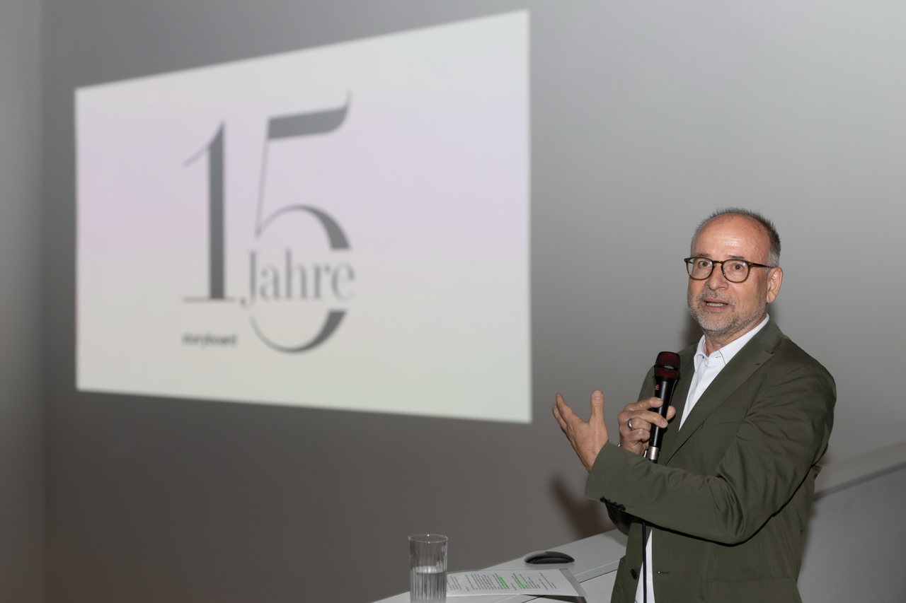 Dr. Markus Schönmann spricht mit Mikrofon vor einer Leinwand mit dem 15-Jahre-storyboard-Logo