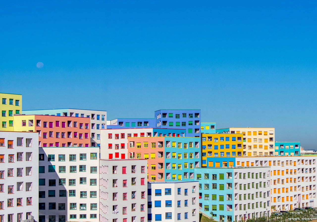 Eine Häuserfont aus etwa fünfzehn bunten rechteckigen Hochhäusern. Je Haus sind gleichmäßig eckige Fenster verbaut.