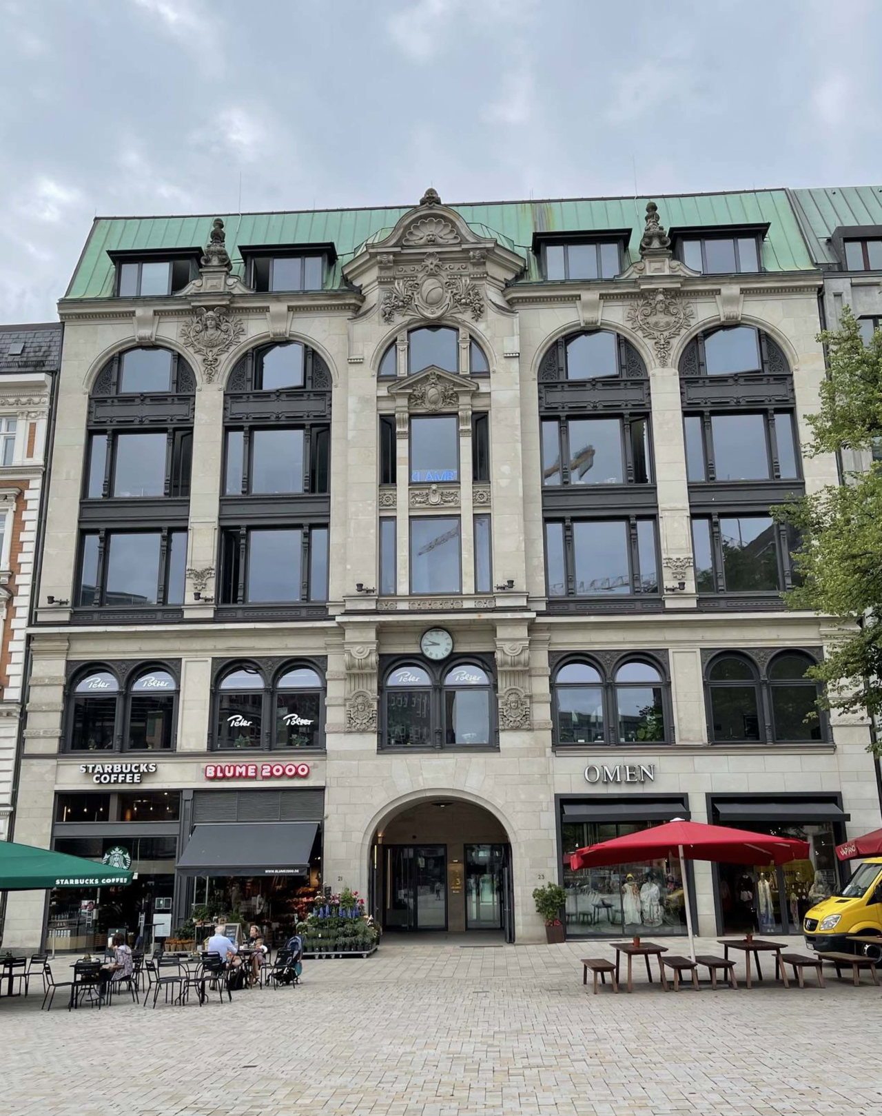Historisches Geschäftshaus mit Kupferdach und Straßencafés an einem gepflasterten Platz