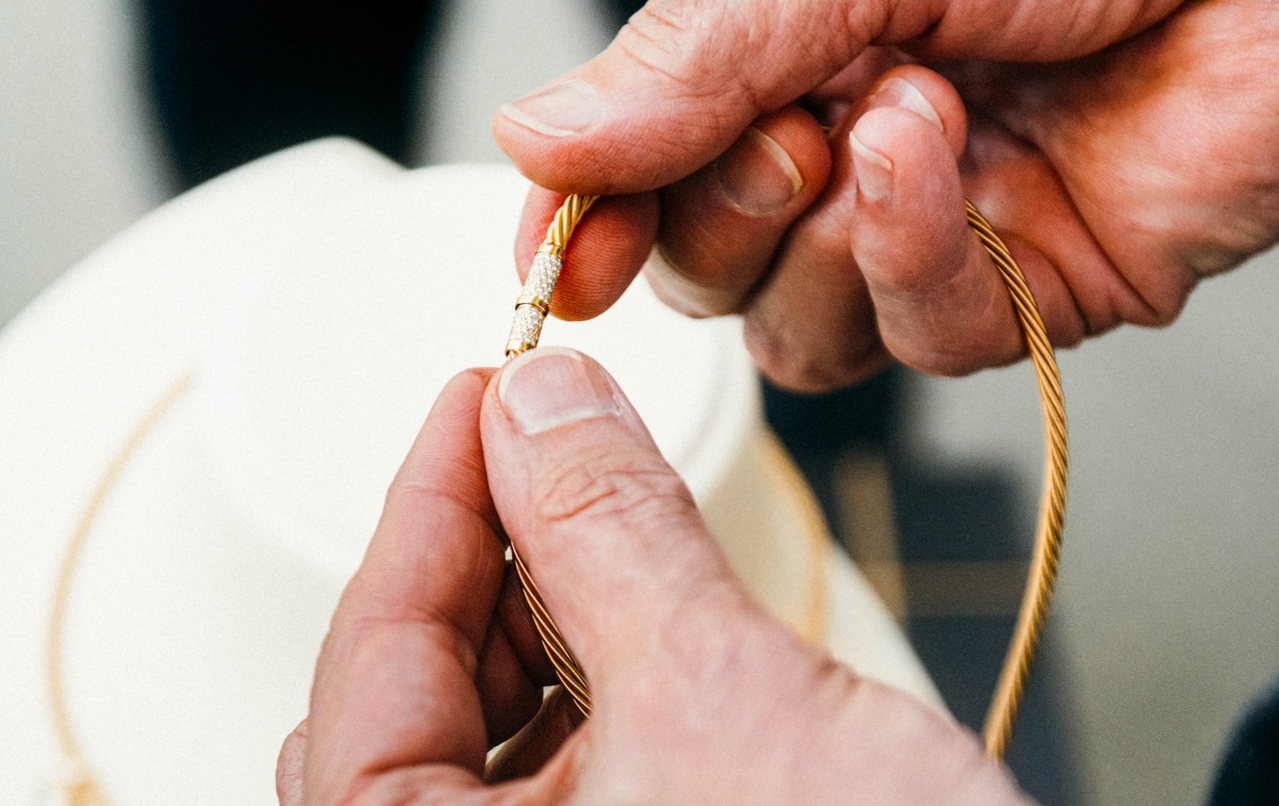 Zwei Händen halten ein goldenes Wellendorff-Collier mit Drehkomfortschließe, der Schmuckverschluss ist mit kleinen Edelsteinen besetzt.