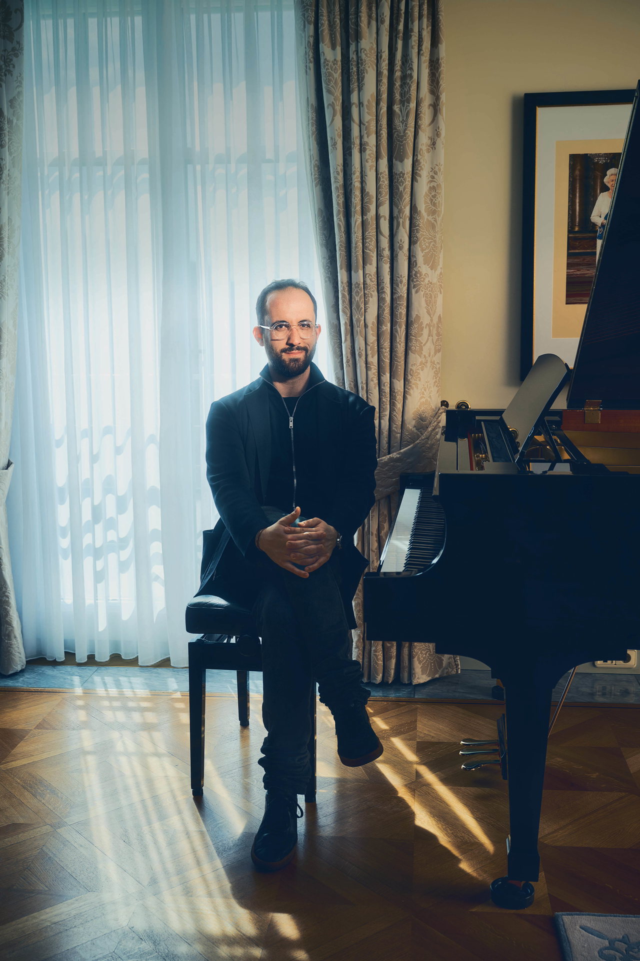 Porträtfoto von Pianist Igor Levit, der in einer Suite des Hotels Adlon Berlin an einem schwarzen Klavier sitzt