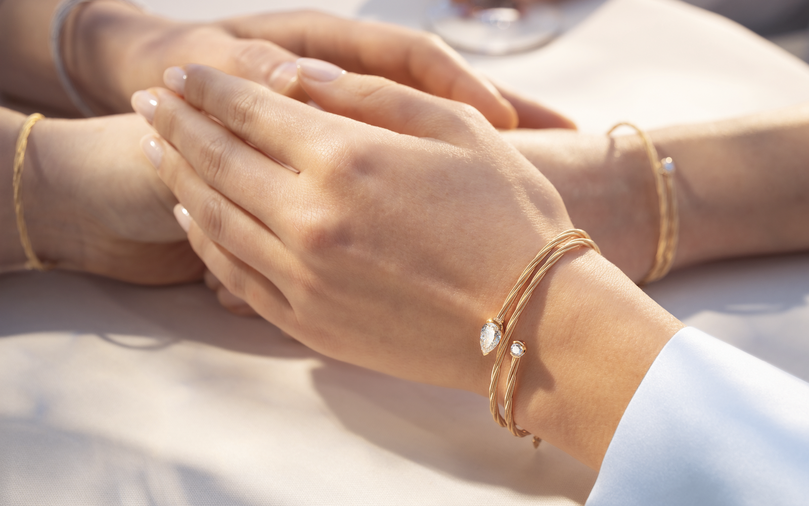 Nahaufnahme der Händen von zwei Frauen, die sich berühren und an beiden Handgelenken filigrane goldene Wellendorff-Armbänder mit Diamanten tragen