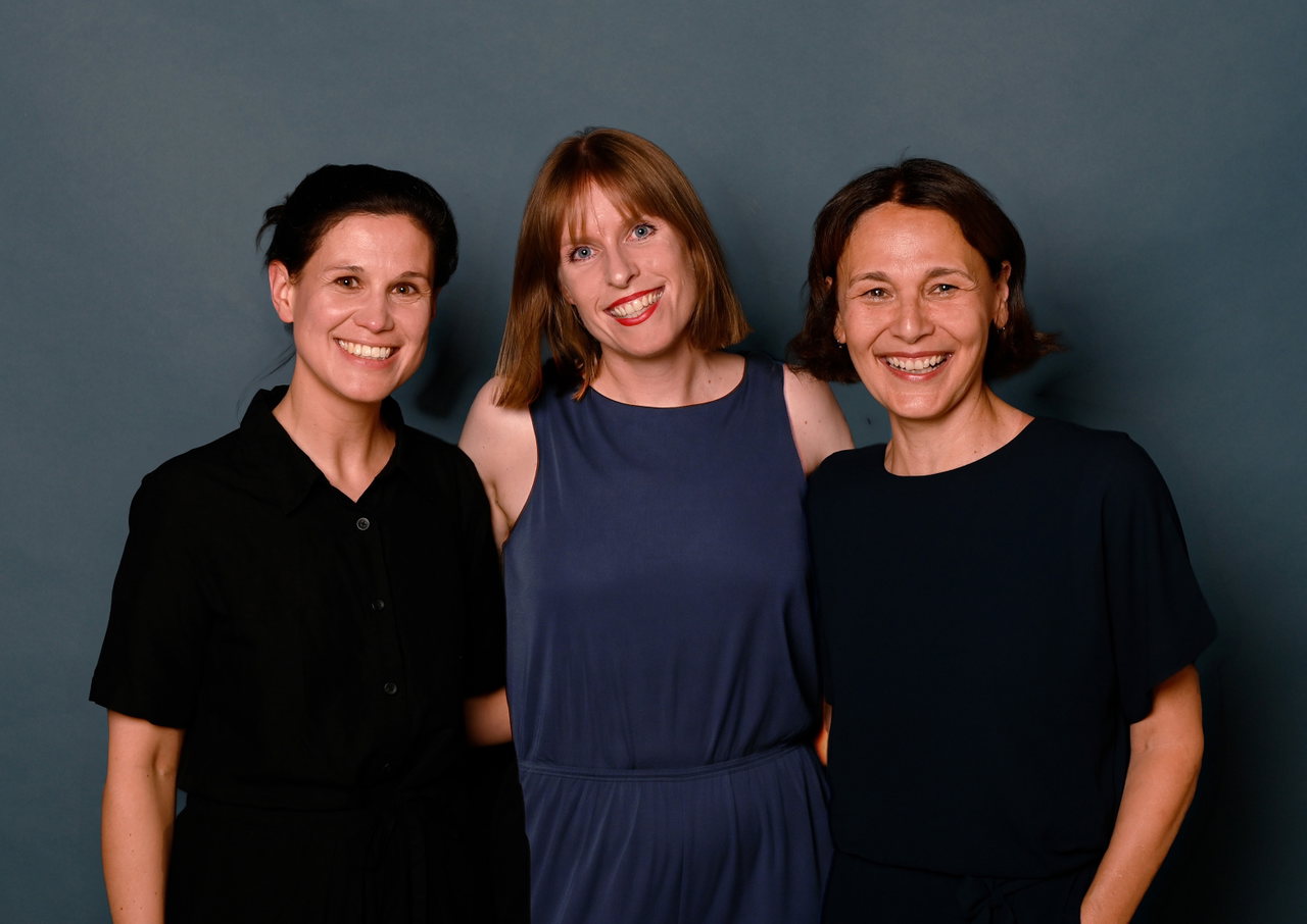 Marlene Irausek, Sandra Djajadisastra und Stefanie Lindner lächeln vor dunkelblauem Hintergrund