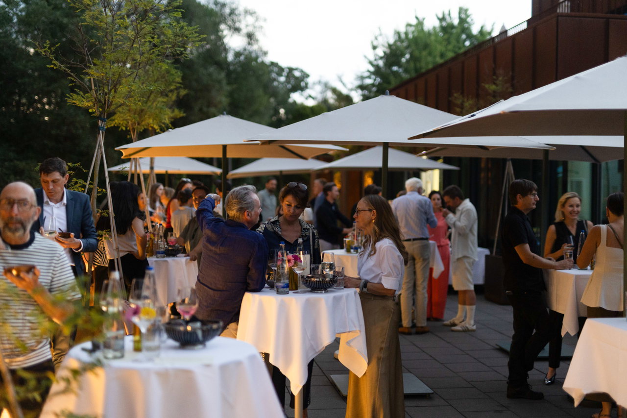Gäste an Stehtischen mit weißen Tischdecken und Sonnenschirmen beim abendlichen Sommerfest