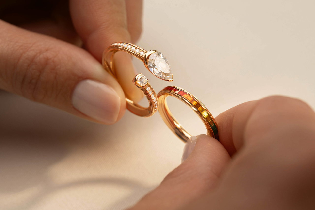 Nahaufnahme von zwei Wellendorff-Ringen, die von zwei Händen gehalten werden: der goldene Ring DIAMANTTROPFEN und ein farbig emaillierter Bandring