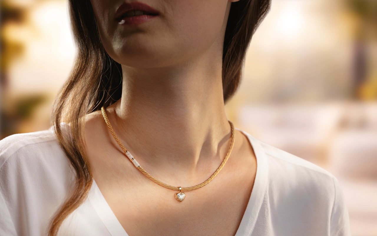 Eine Frau trägt ein goldenes Wellendorff-Collier mit einem herzförmigen Anhänger um den Hals.
