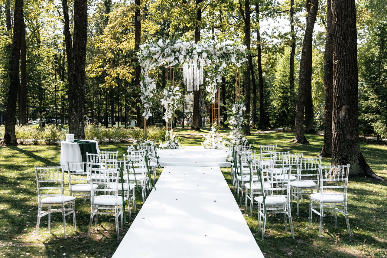 wedding-ceremony-with-white-chairs-path-arch-white-flowers-edge-forest