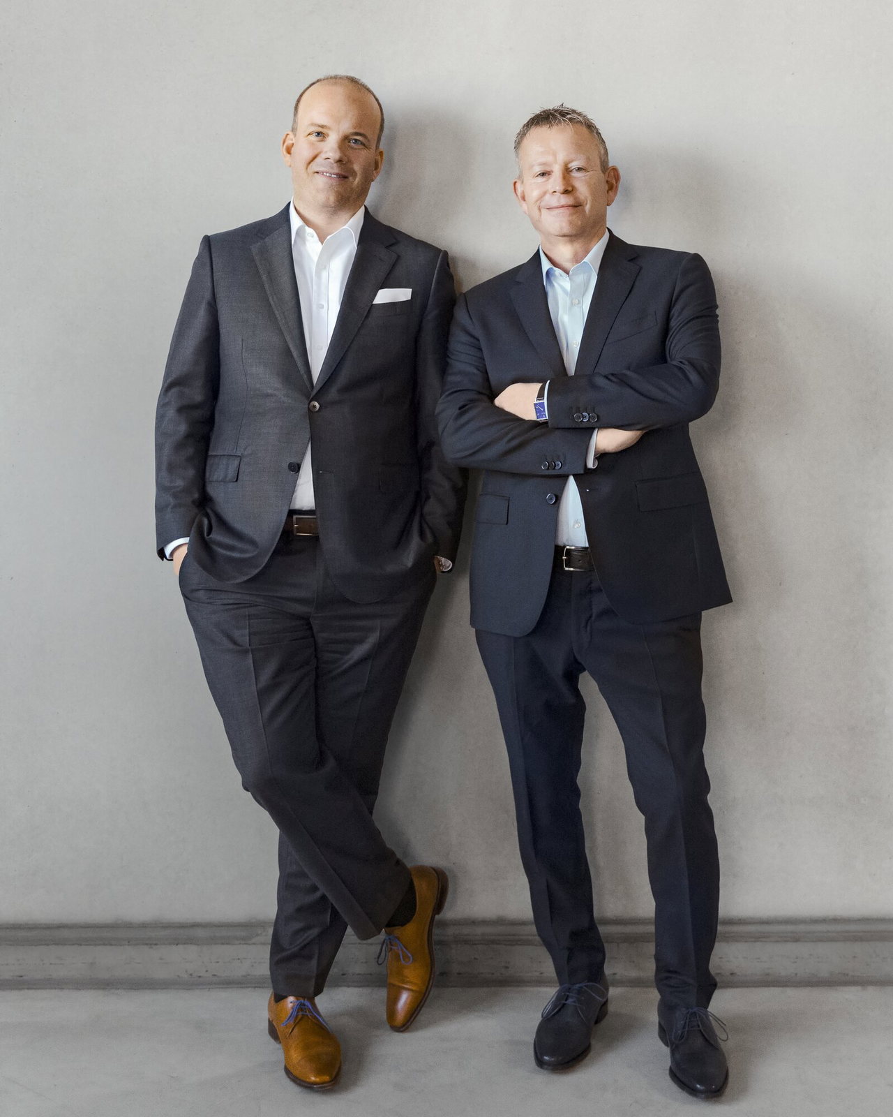 Die geschäftsführenden Gesellschafter Jochen Geis und Hans-Wolfgang Geis stehen an eine Betonwand gelehnt