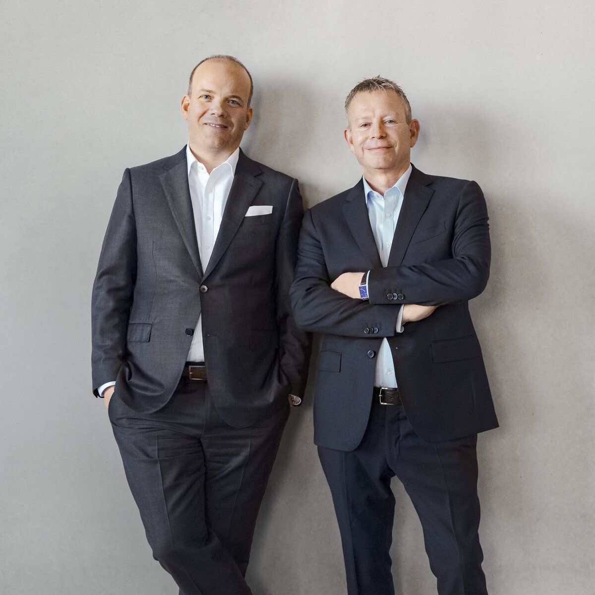 Die geschäftsführenden Gesellschafter Jochen Geis und Hans-Wolfgang Geis stehen an eine Betonwand gelehnt