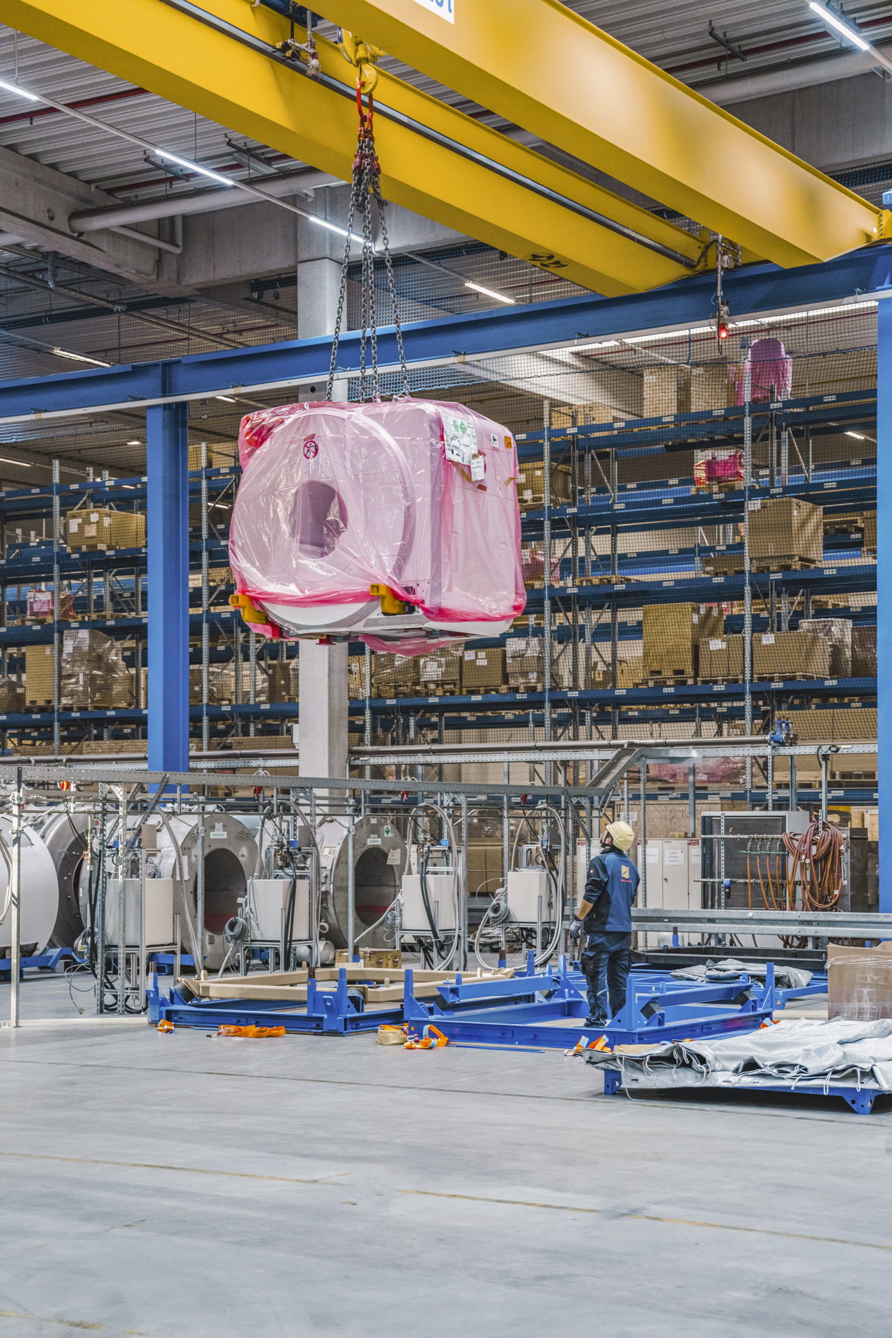 Ein rosa verpacktes MRT-System hängt am Hallenkran über den Lagerplätzen in Frauenaurach