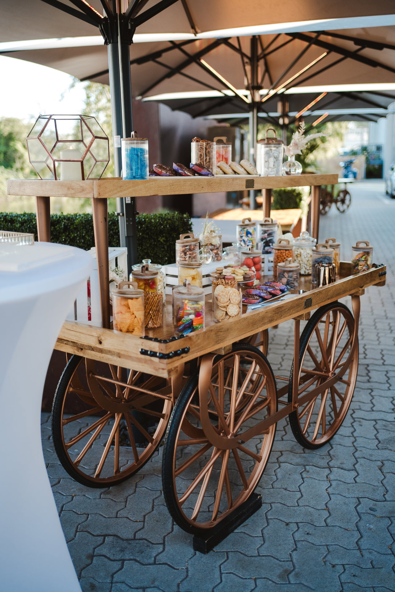 Holzwagen mit Gläsern voller Süßigkeiten unter Sonnenschirmen