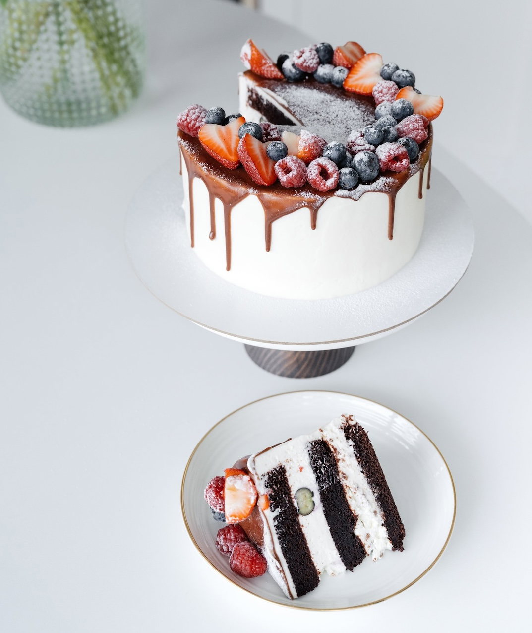Fertige Beerentorte mit Schokoladenglasur, davor ein angeschnittenes Stück auf einem Teller