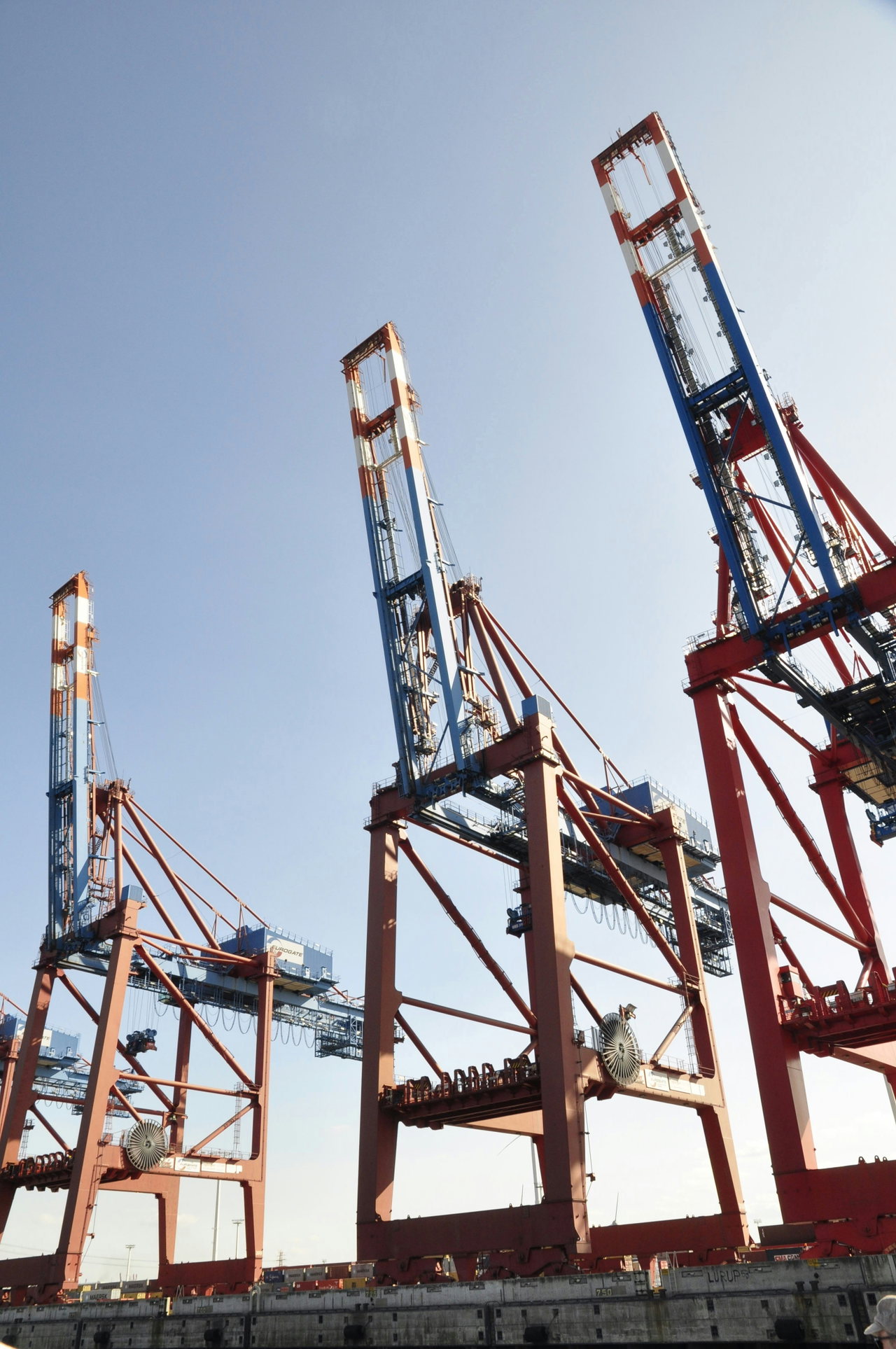 Drei rot-weiße Containerbrücken vor blauem Himmel
