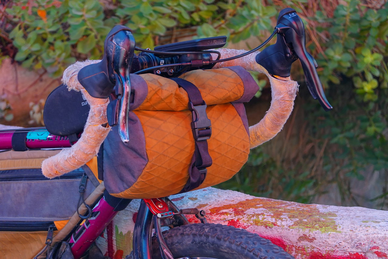 Orangefarbene Lenkerrolle mit Riemen am Rennlenker eines Gravelbikes, dahinter grünes Laub
