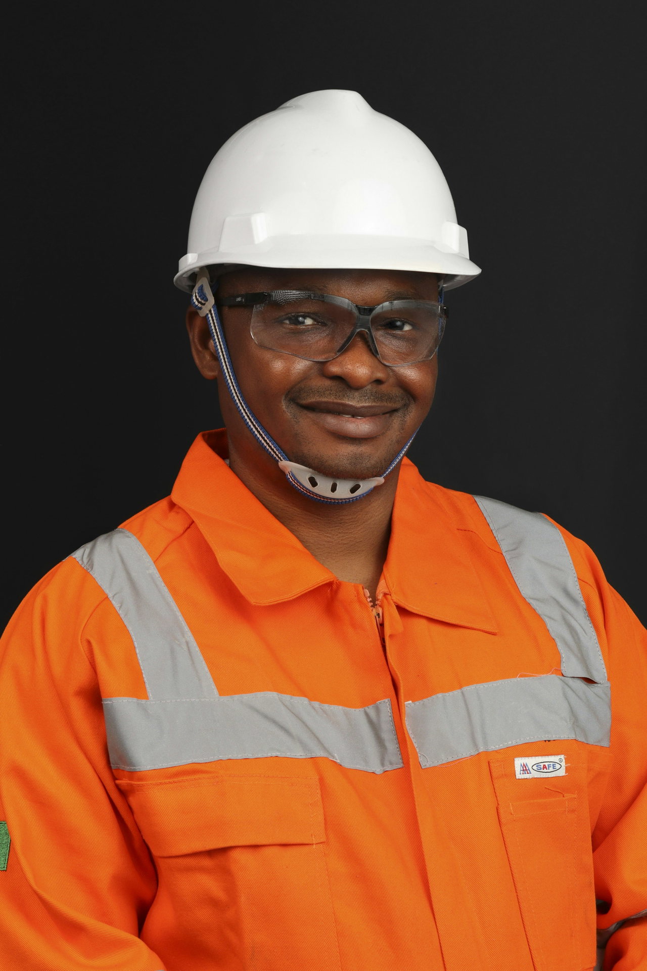 Lächelnder Techniker mit weißem Schutzhelm, Schutzbrille und orangefarbener Warnschutzkleidung.
