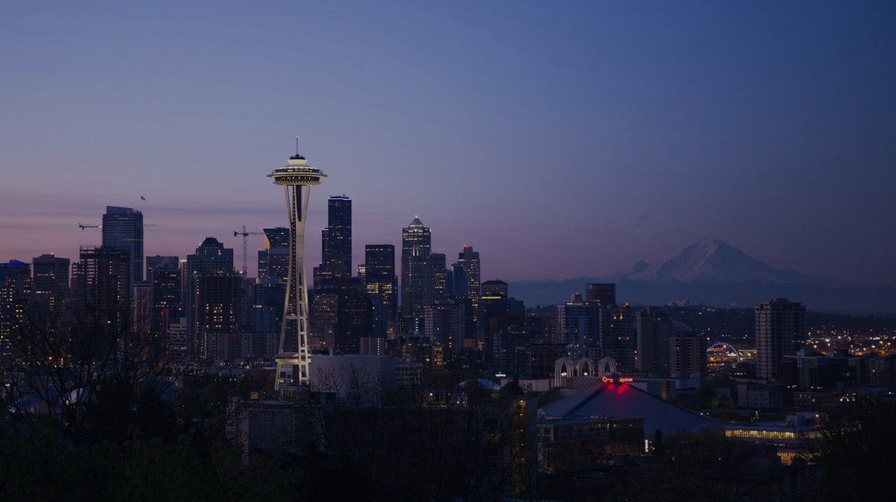 Skyline von Seattle in der Abenddämmerung mit der Space Needle, dahinter der schneebedeckte Mount Rainier