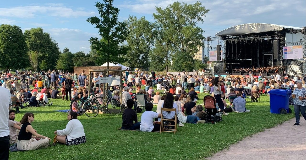 Menschen sitzen bei einem Open-Air-Konzert auf einer Wiese vor der Bühne