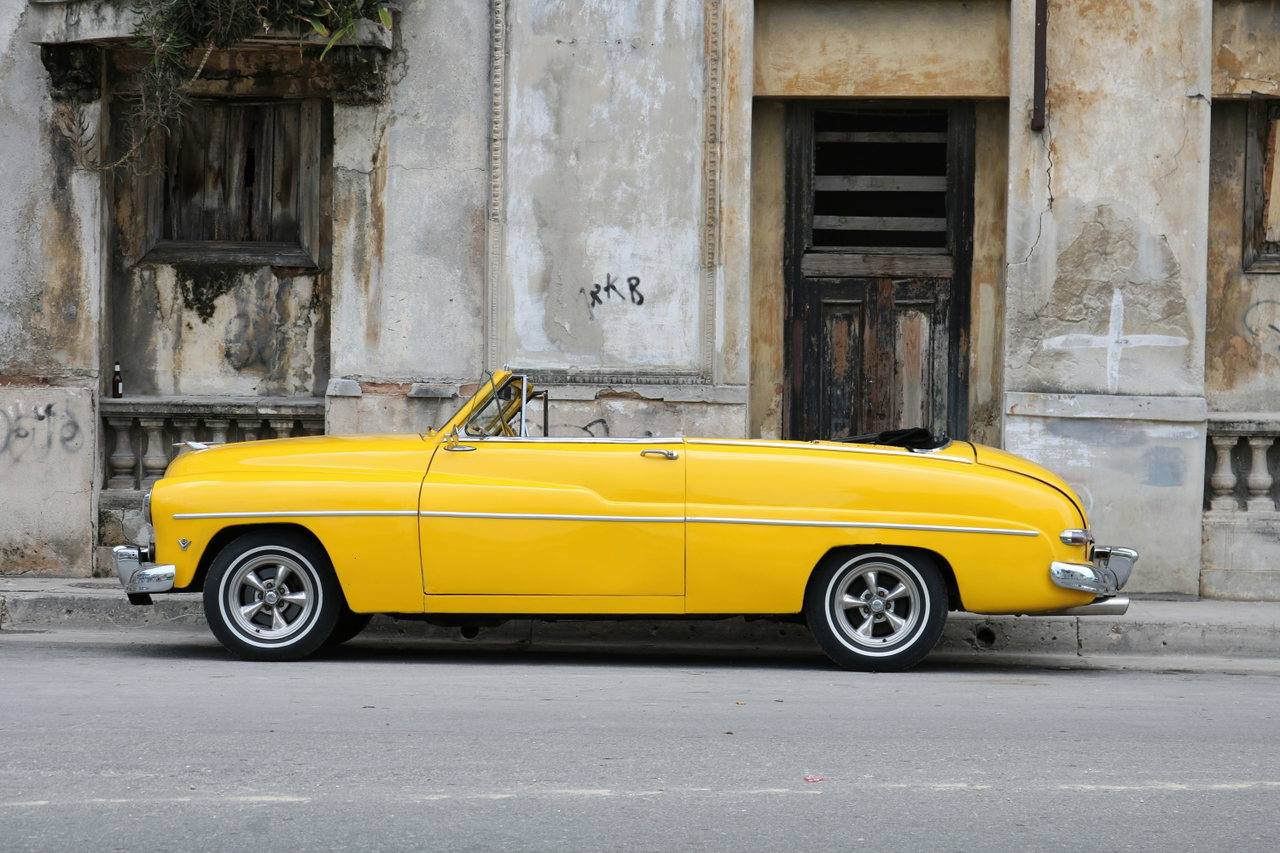 Gelber Oldtimer vor einer verwitterten Fassade in Havanna
