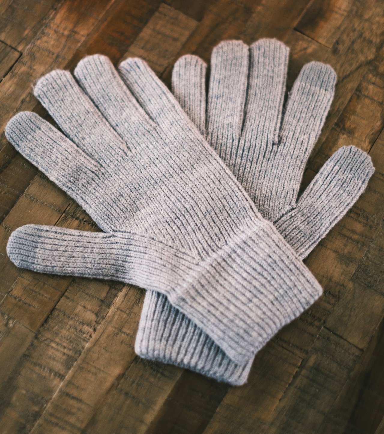 Paar graue Strickhandschuhe mit Rippbündchen auf dunklem Holztisch