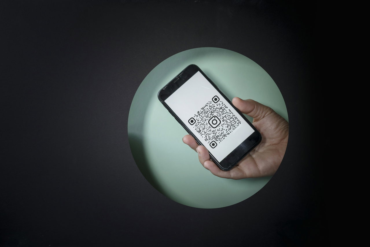 Hand holding a smartphone with a QR code on the display against a dark background