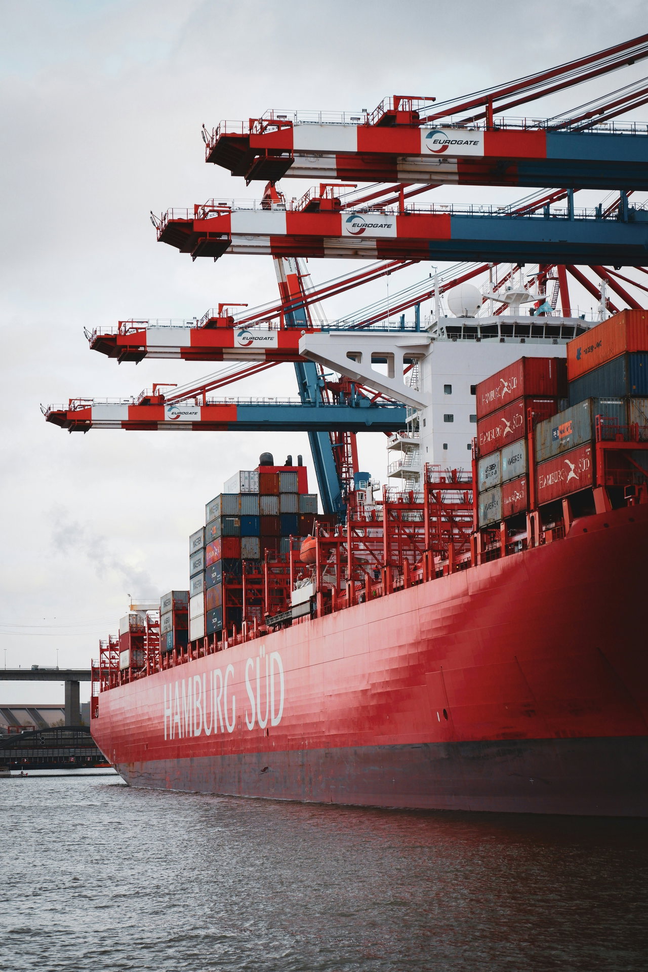 Rot-weißes Containerschiff unter den Containerbrücken eines Terminals