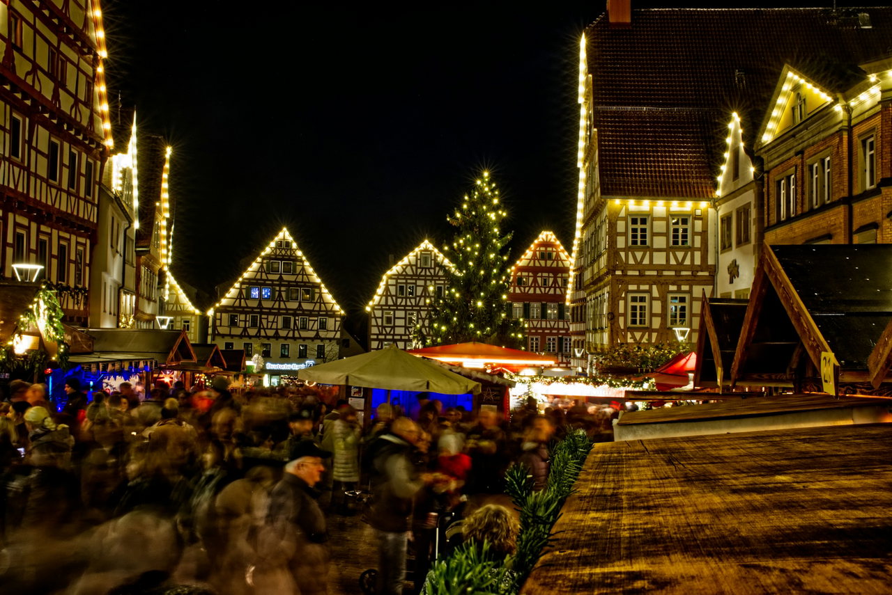 Weihnachtsmarkt am Abend mit beleuchteten Fachwerkhäusern, Tannenbaum und vielen Besuchern auf dem Platz