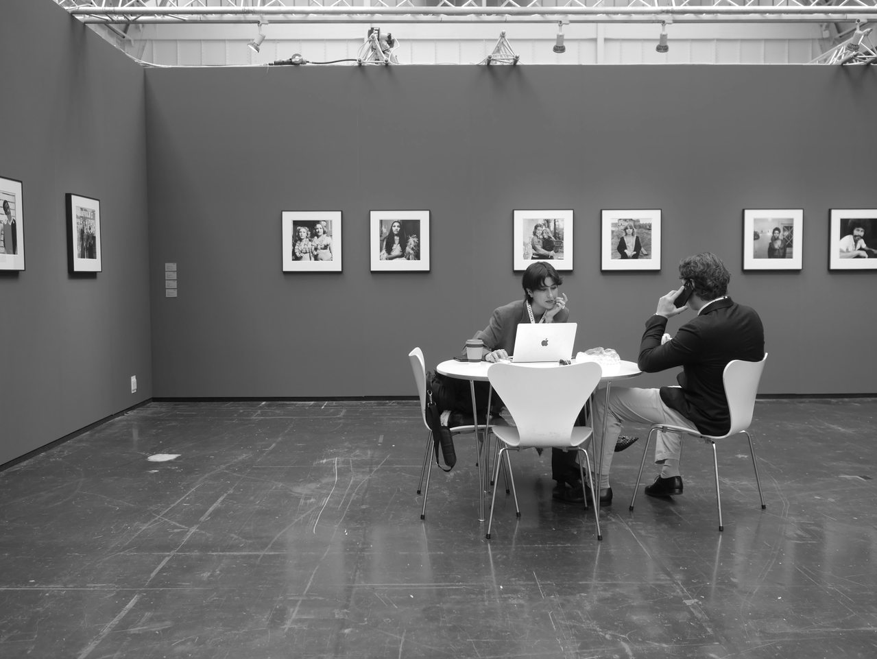 Zwei Menschen im Gespräch an einem Tisch in einer großen Ausstellungshalle mit gerahmten Fotografien