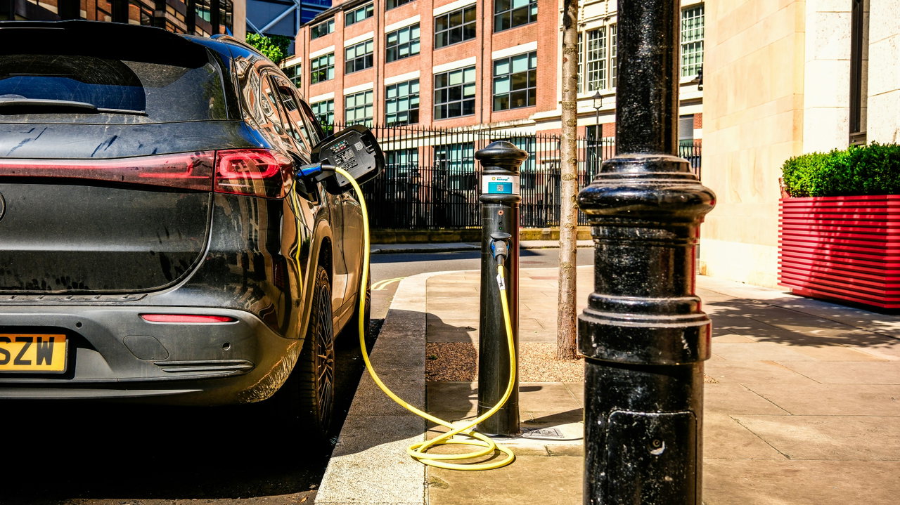 Ein dunkles Elektroauto lädt an einer Ladesäule am Straßenrand
