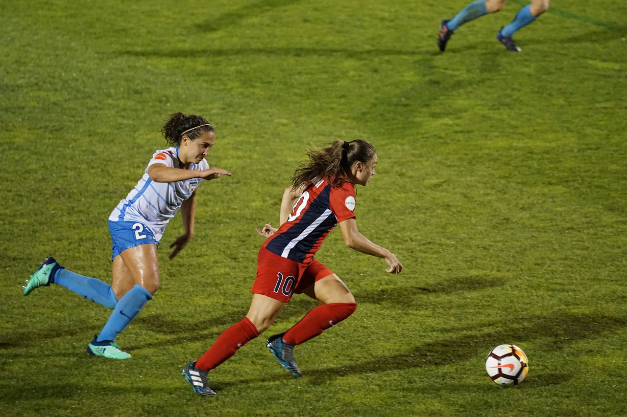 Zwei Fußballerinnen in hellblauem und rotem Trikot sprinten bei einem Spiel dem Ball hinterher