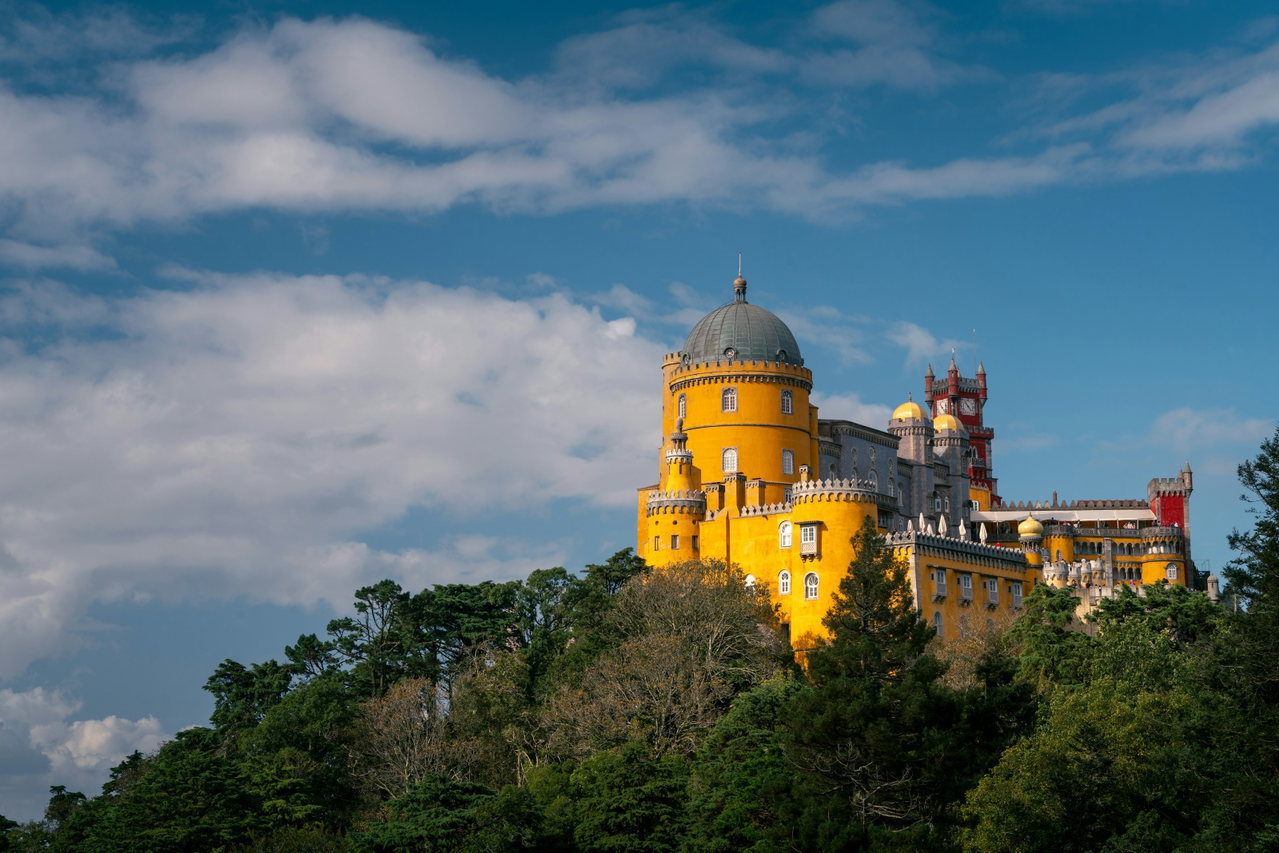 Der gelbe Pena-Palast von Sintra thront über dem grünen Wald vor blauem Himmel mit Wolken