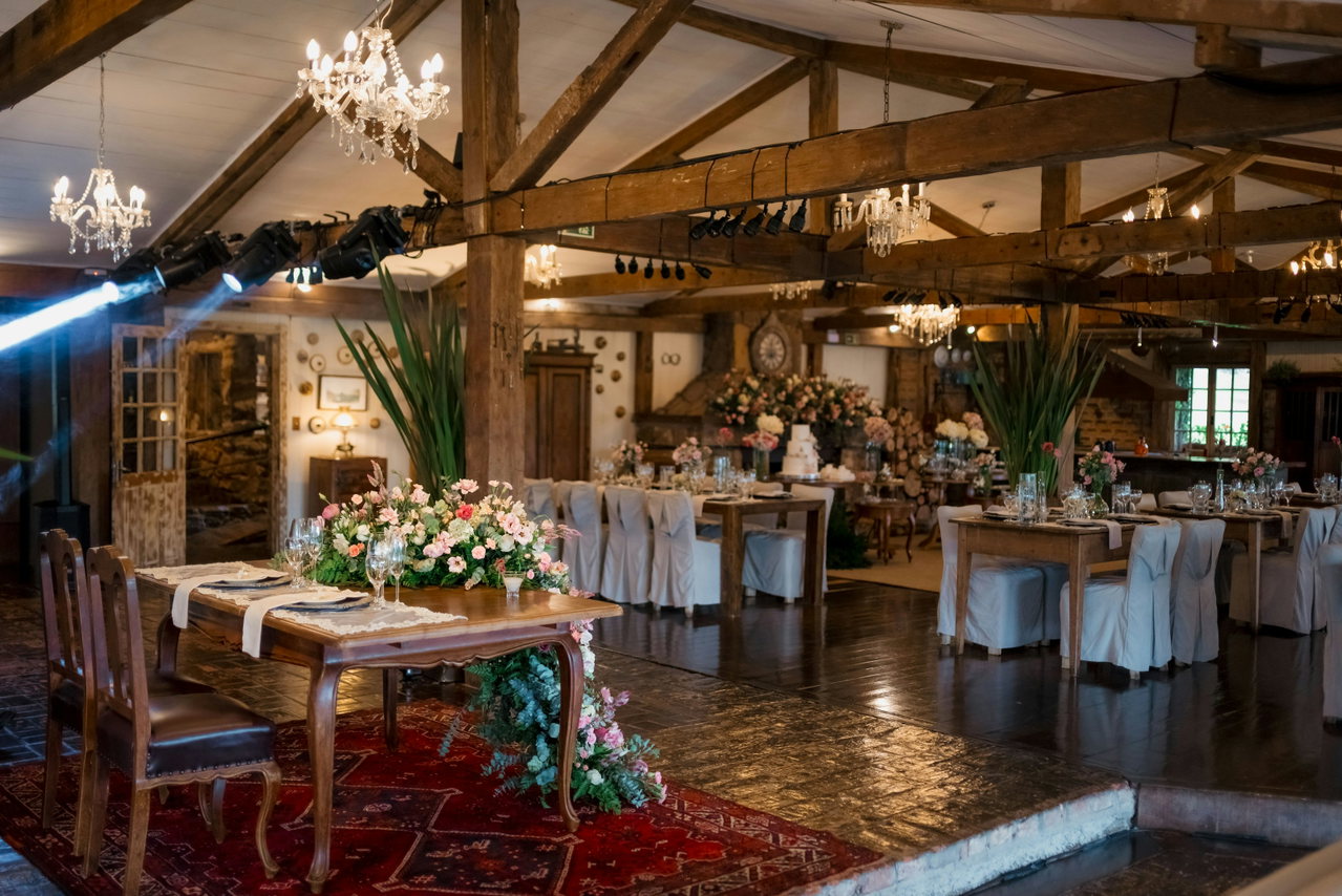 Festlich gedeckter Saal mit Holzbalken, Kronleuchtern, Lichterketten und Blumen vor dem Fest