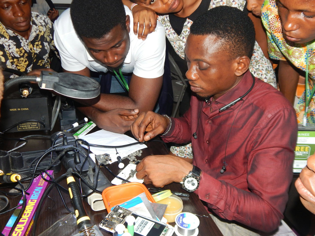 Menschen drängen sich im Repair-Café um einen Tisch und reparieren gemeinsam ein elektronisches Gerät