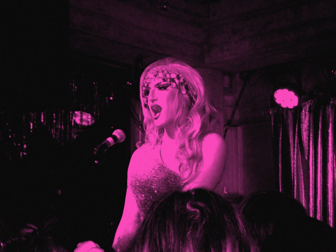 Symbolfoto: Drag-Performerin im Kostüm singt ins Mikrofon, Schwarzweiß mit Magenta-Duplex