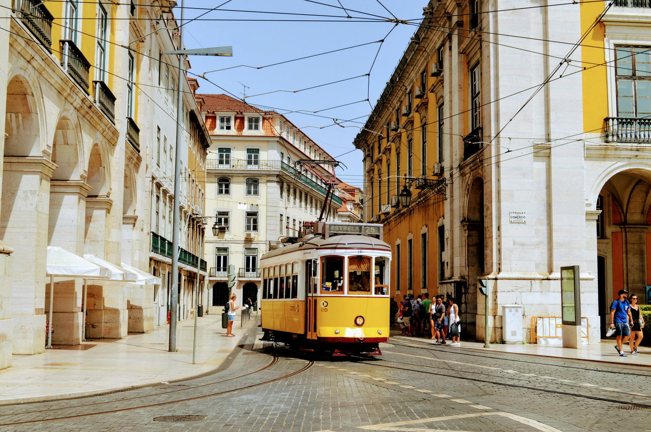 Gelbe Straßenbahn fährt durch eine sonnige Altstadtstraße in Lissabon zwischen gelben und weißen Häusern
