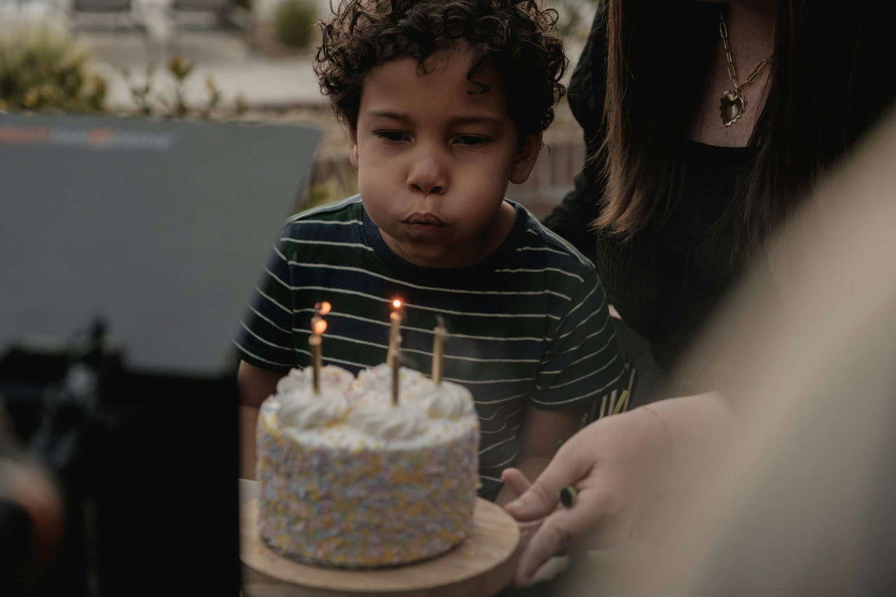 Kleiner Junge mit Locken und gestreiftem Shirt pustet über einer Torte die Kerzen aus