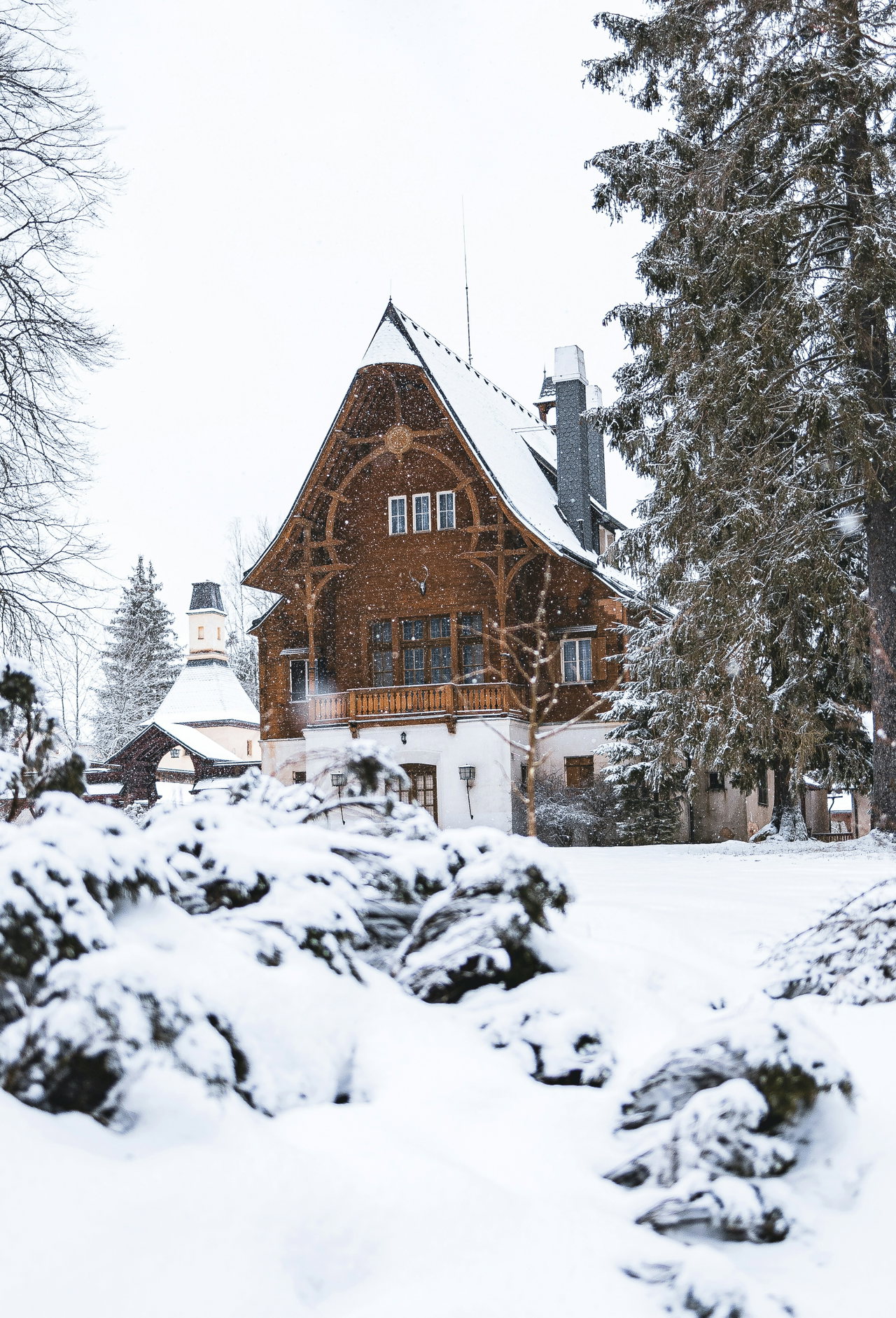 Holzverkleidetes Landhaus mit Schieferdach und Turmerker, umgeben von tief verschneiten Fichten im Winterwald