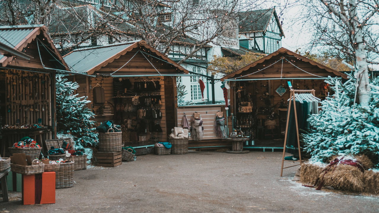 Kleine Holzhütten eines ländlichen Weihnachtsmarkts mit Tannen, Strohballen und Fachwerkhäusern im Hintergrund