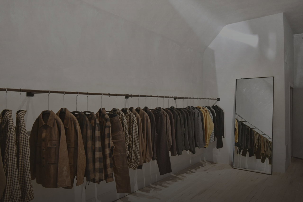 Heller, minimalistischer Modeladen mit langer Kleiderstange voller brauner Jacken und Mäntel, Spiegel an der Wand