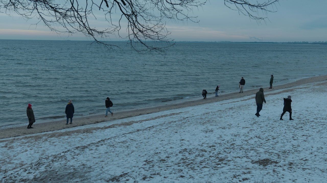 Spaziergänger am verschneiten Ostseestrand unter grauem Winterhimmel