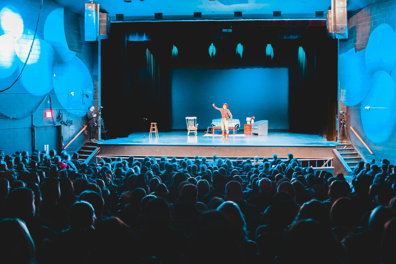 Blick über das Publikum auf eine blau beleuchtete Theaterbühne