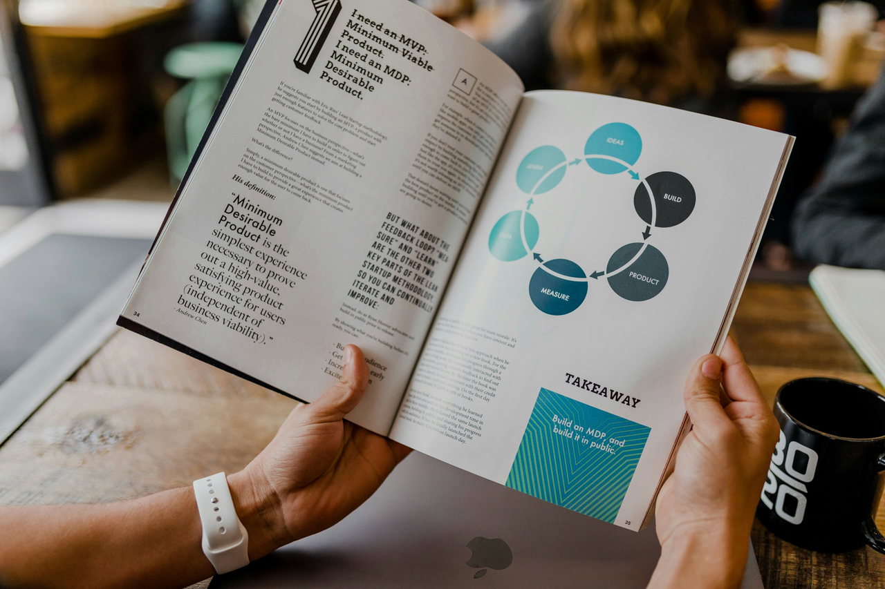 Hände halten eine Zeitschrift mit einer Infografik in Türkis, im Hintergrund ein Laptop