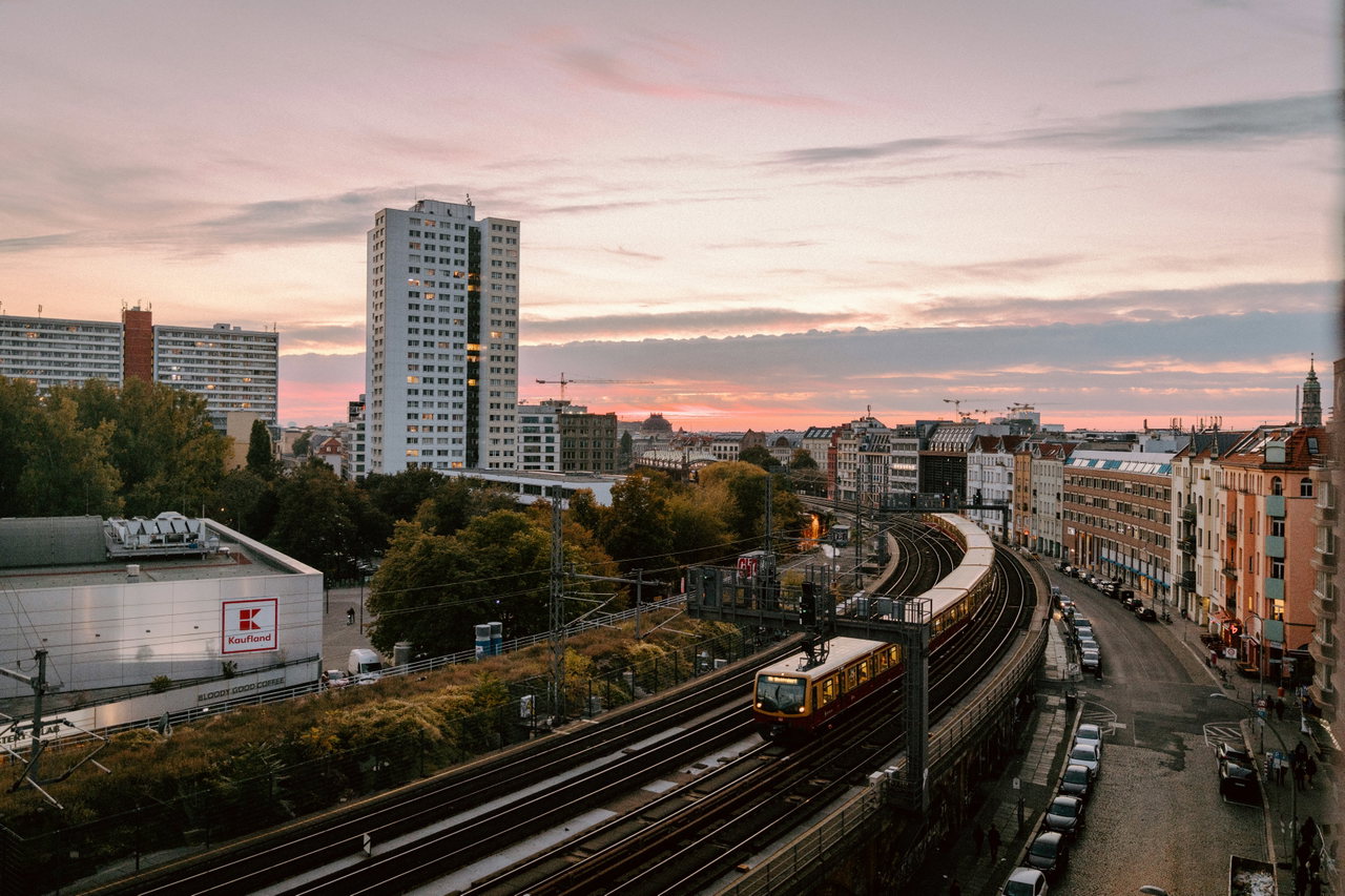 S-Bahn-Zug in einer Gleiskurve zwischen Hochhaus und Altbauten, Morgenhimmel in Orange und Rosa