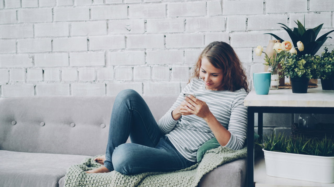Frau liest entspannt auf dem Sofa auf ihrem Smartphone und lächelt