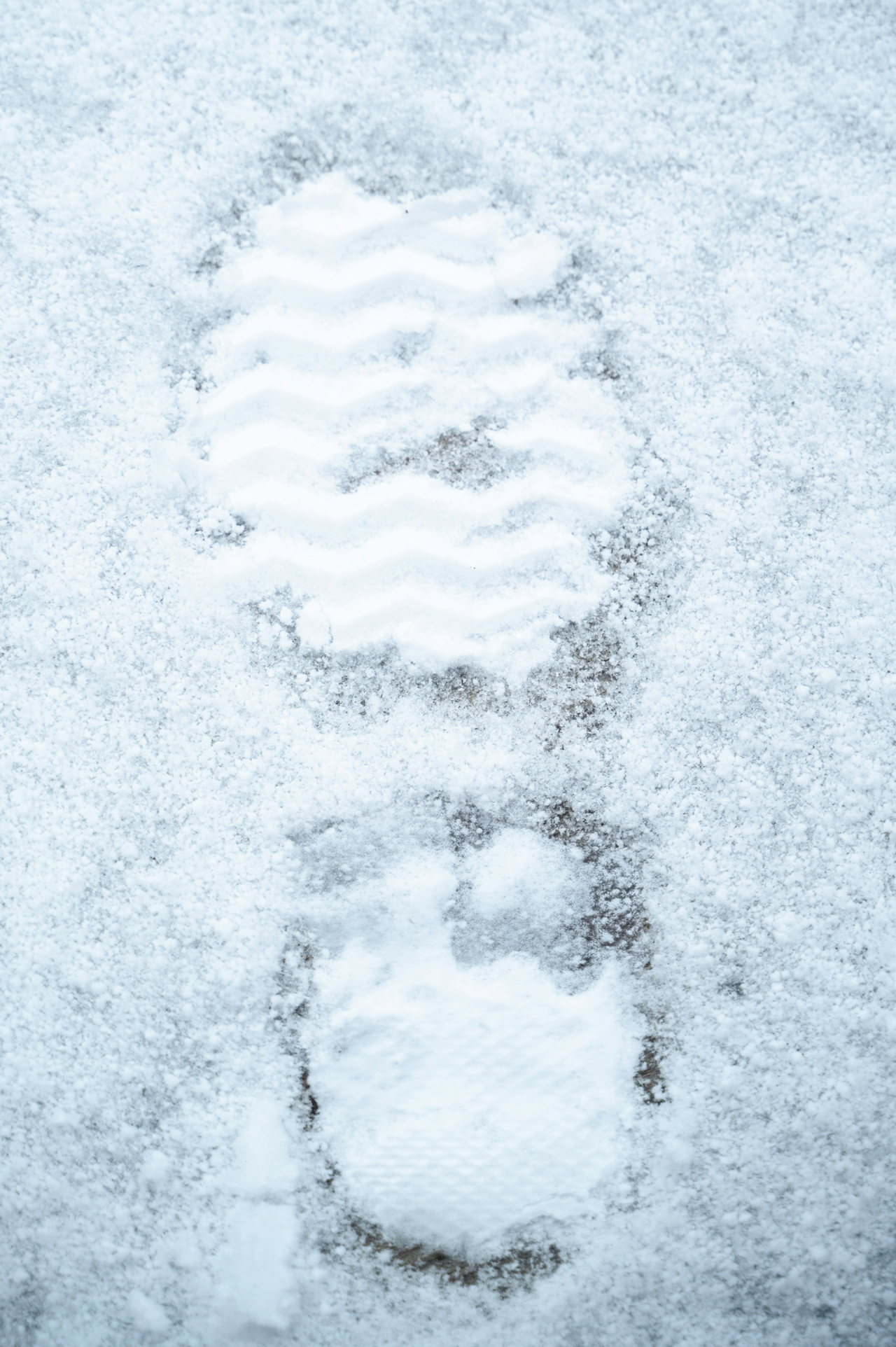 Nahaufnahme eines Stiefelabdrucks im frischen Schnee, weiches kühles Licht