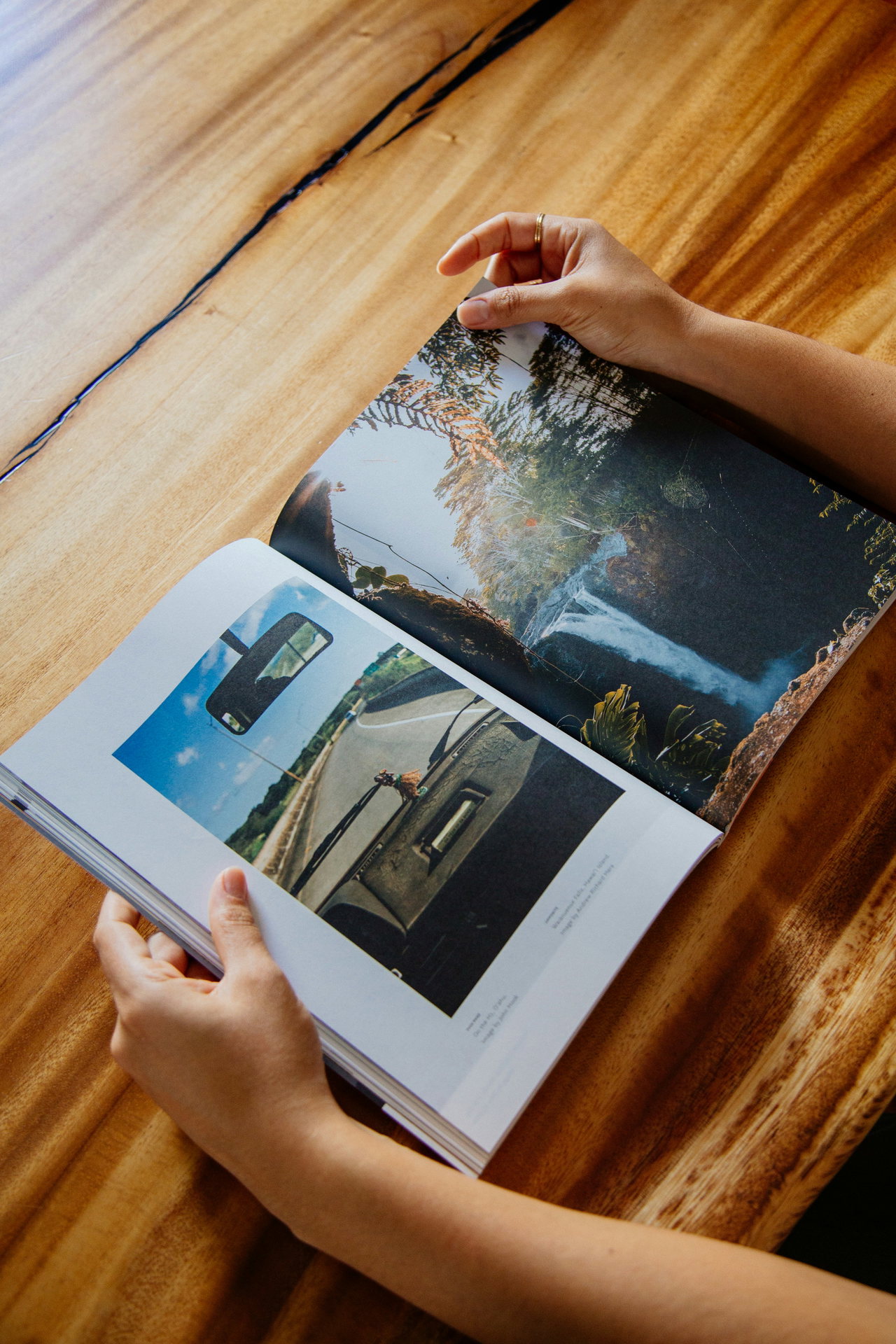 Hände halten ein aufgeschlagenes Magazin mit großformatigen Landschaftsfotos über einem Holztisch