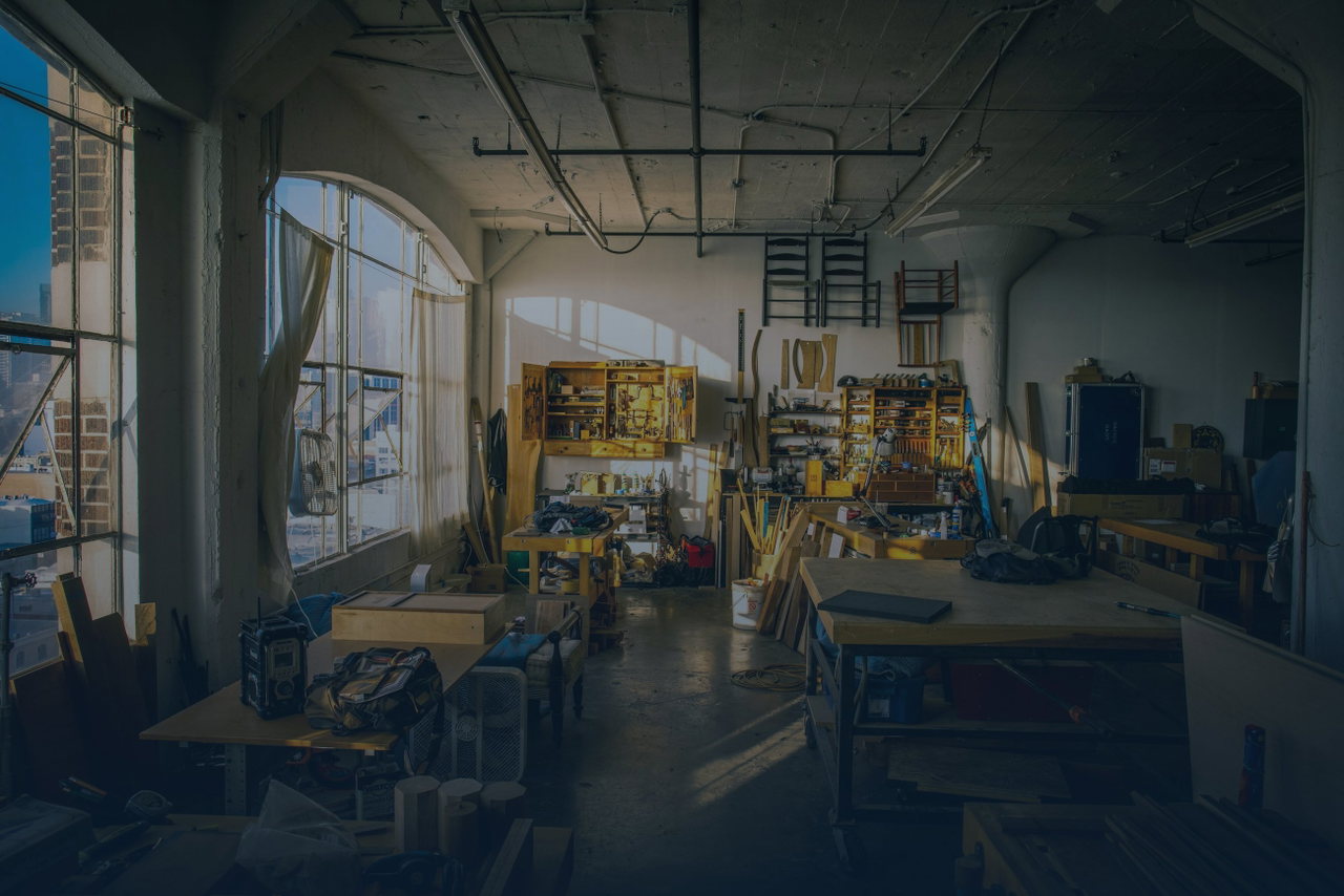 Helle Werkstatt mit hohen Bogenfenstern, Werkbänken und Materialregalen im warmen Tageslicht