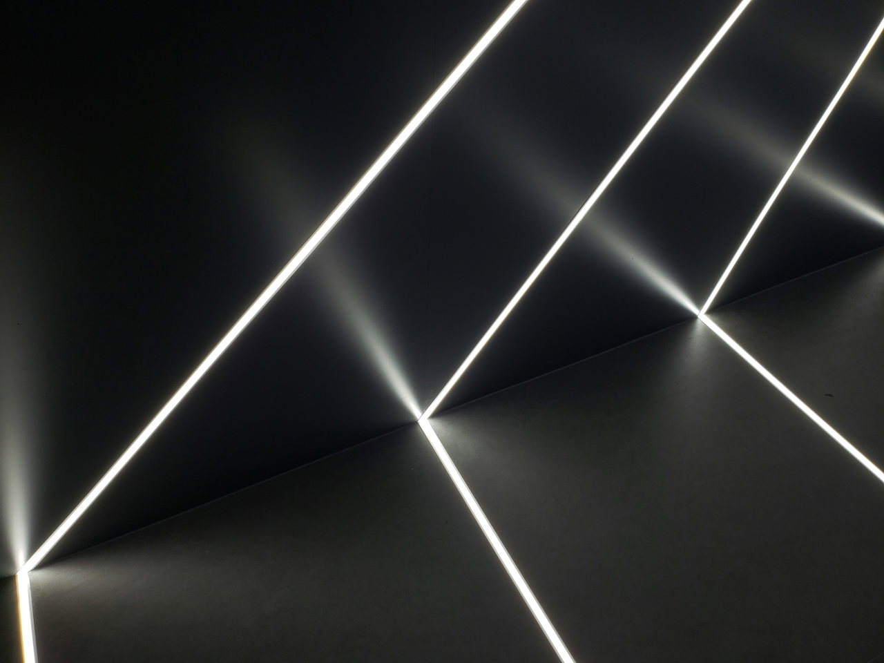 Dünne weiße Lichtlinien auf dunklem Hintergrund, die sich in einem Raum kreuzen