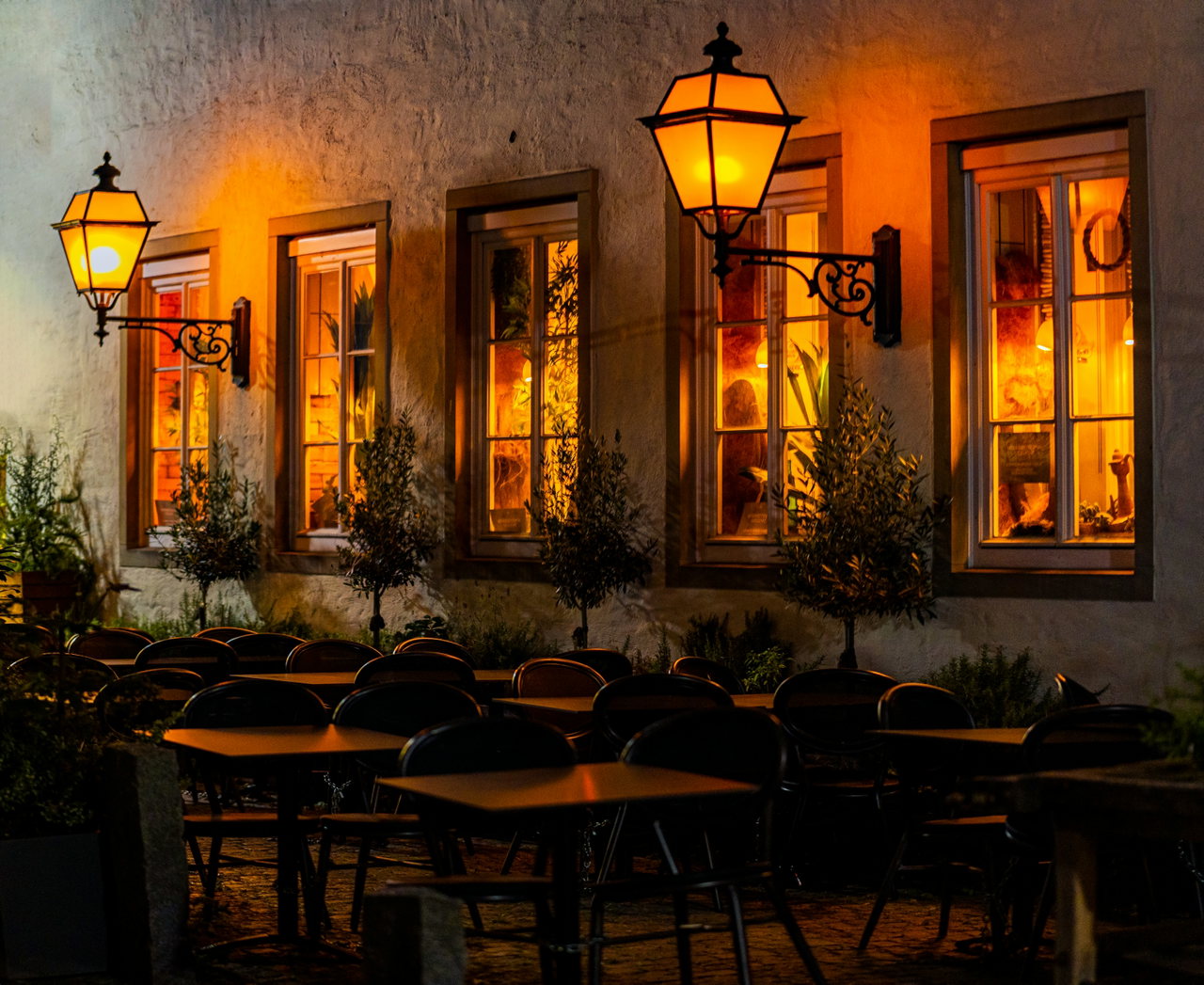 Café-Terrasse am Abend mit leuchtenden Laternen, Fenstern und leeren Stühlen