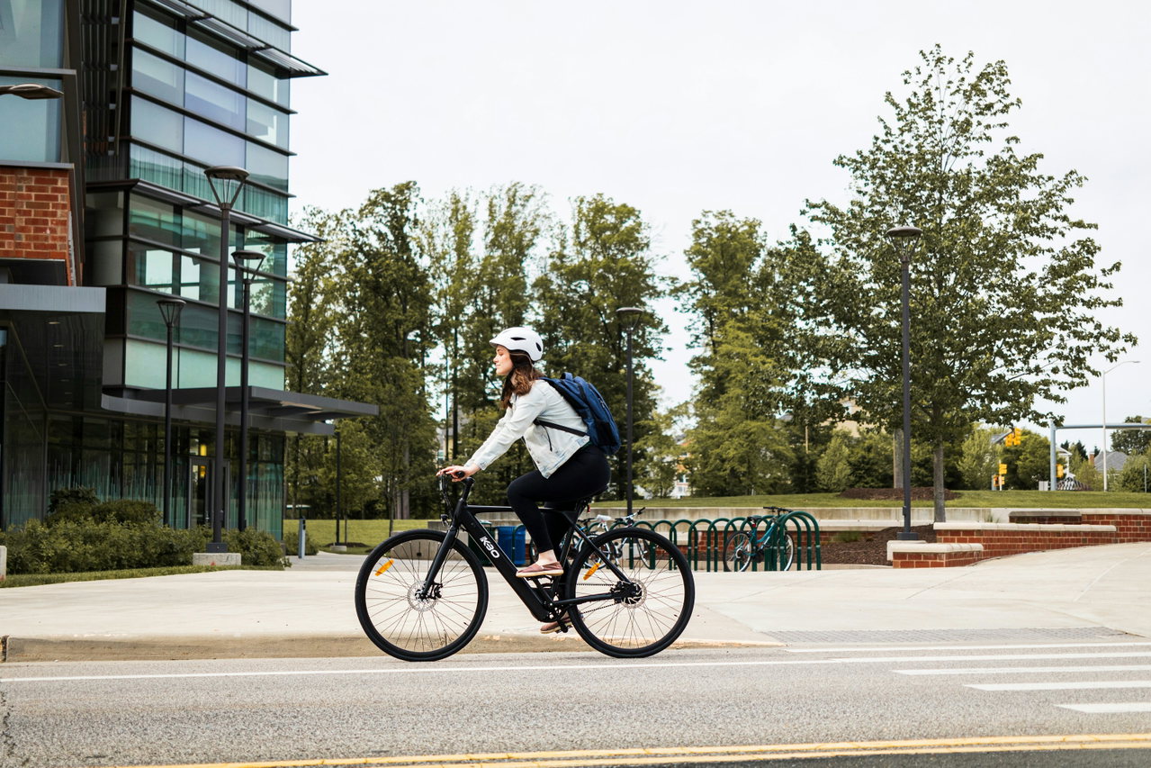 Frau mit Helm fährt auf einem E-Bike an einem modernen Bürogebäude vorbei.